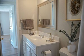 A bathroom with a white sink, a mirror, a toilet, and a plant.
