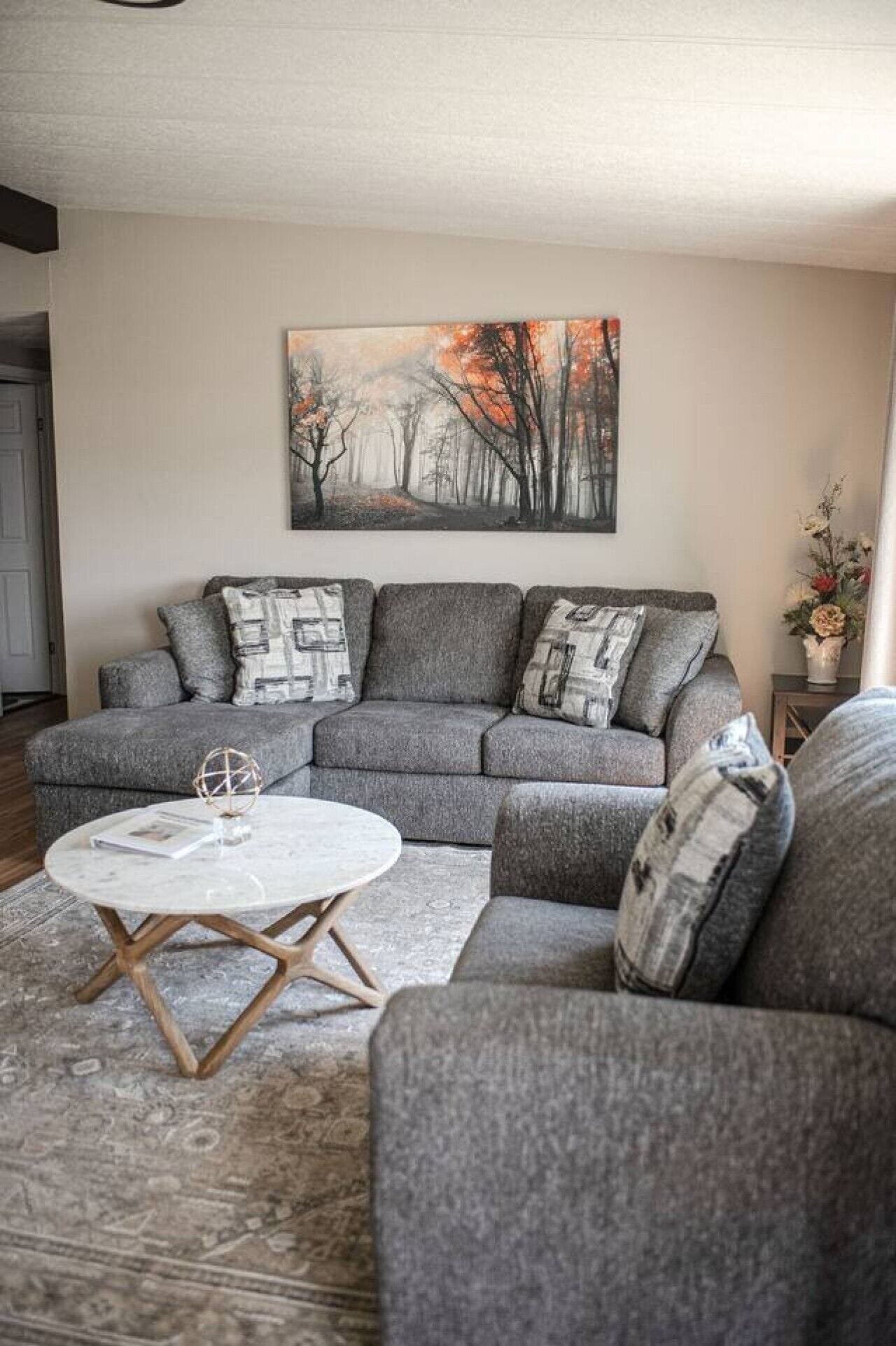 A living room with a grey sectional sofa, a round coffee table, and a painting on the wall.