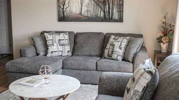 A living room with a grey sectional sofa, a round coffee table, and a painting on the wall.