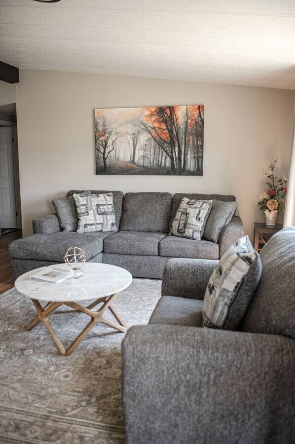 A living room with a grey sectional sofa, a round coffee table, and a painting on the wall.