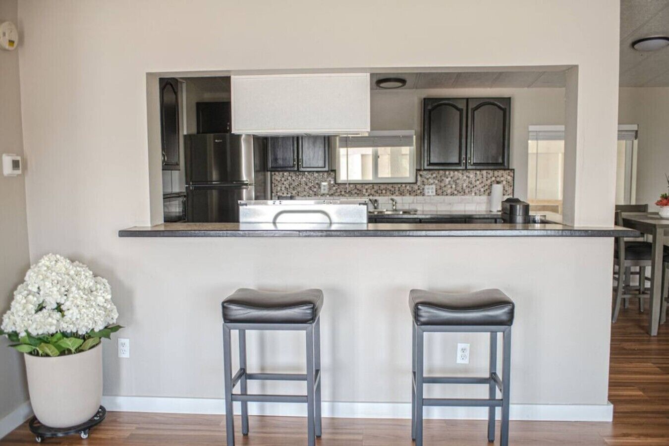 A modern kitchen with a central island, two bar stools, and a potted plant.