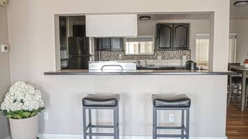 A modern kitchen with a central island, two bar stools, and a potted plant.