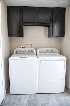 Une buanderie avec deux appareils blancs, un sèche-linge et une machine à laver, placés sous des meubles de rangement aux couleurs sombres.