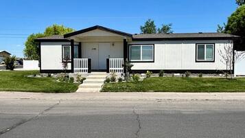 A single-story mobile home with a front porch, a garage, and a small front yard.
