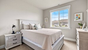 A bedroom with a bed, bedside table, lamp, and a window with a view of houses. - Spacious 3BR Home + Office | Work & Relax (Boardman)