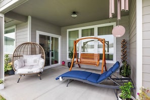 A covered porch with a wicker chair, a swing, and a blue lounge chair.