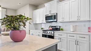 A modern kitchen with white cabinetry, a stainless steel microwave, and a pink vase with a plant. - Spacious 3BR Home + Office | Work & Relax (Boardman)