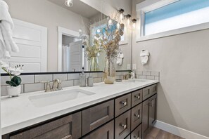 A modern bathroom with dual sinks, a large mirror, and a decorative vase.