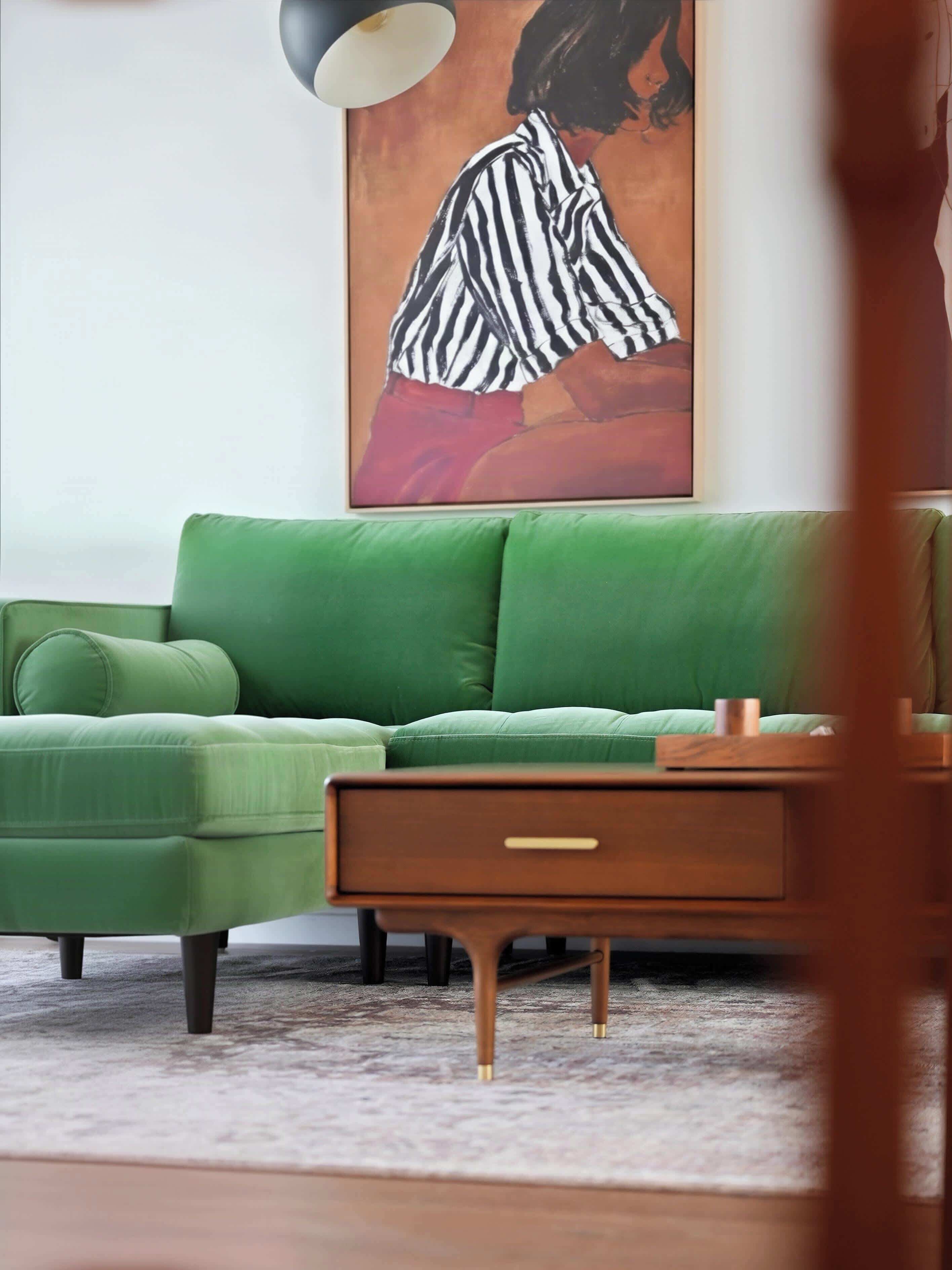 A green sofa, a wooden side table, and a painting on the wall.