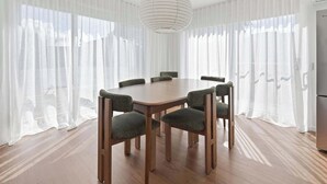 A dining area with a round table and six chairs, large windows with sheer curtains, and a modern pendant light. - Linton, Architect Home Near Mt Panorama (Kelso)