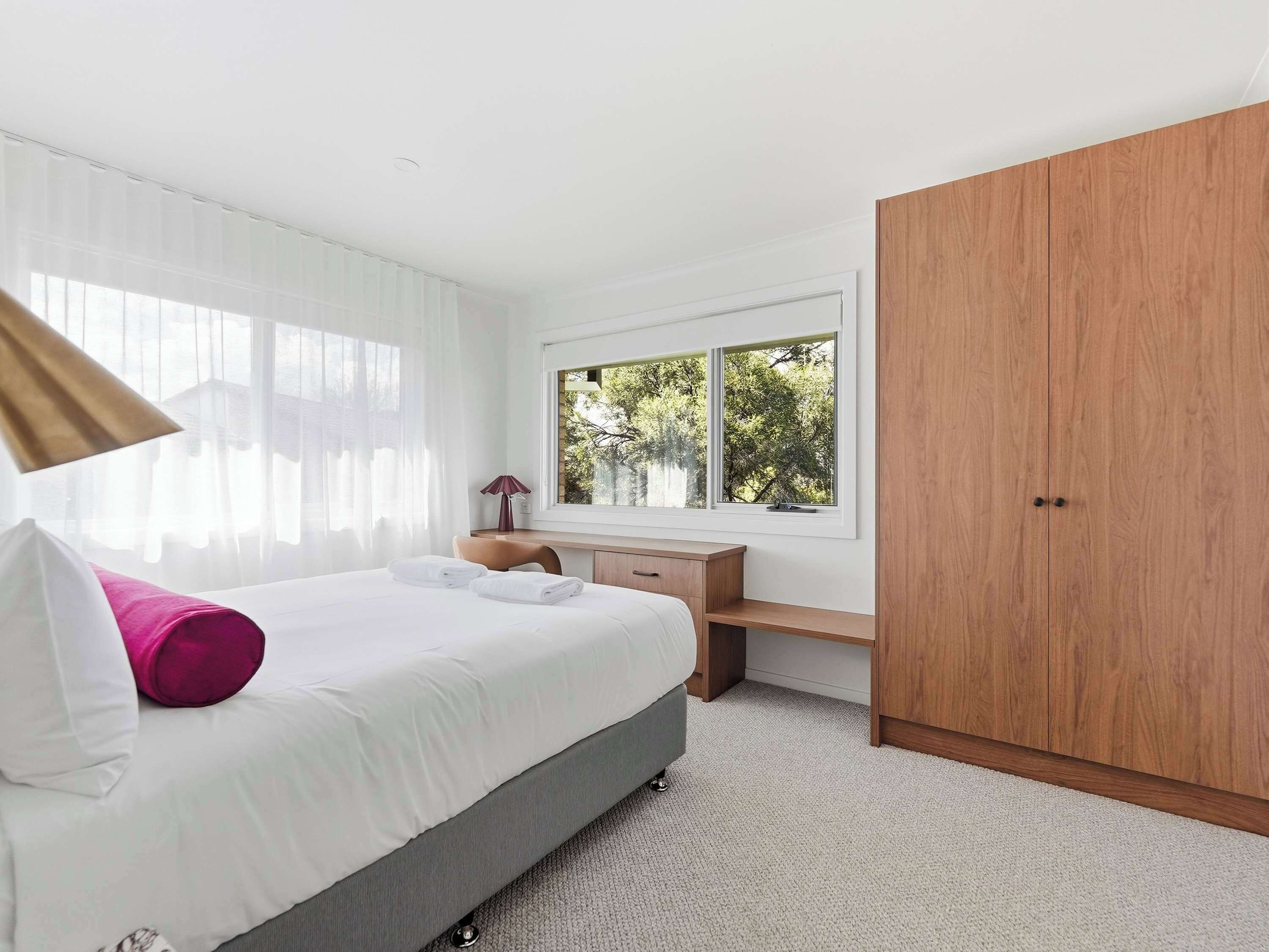 Une chambre d’hôtel avec un lit, un bureau, une armoire et une fenêtre donnant sur des arbres.