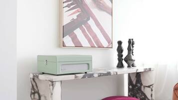 Une pièce comprenant une console dont le plateau est décoré d’un motif imitant le marbre, une radio ancienne et un tableau abstrait encadré.
