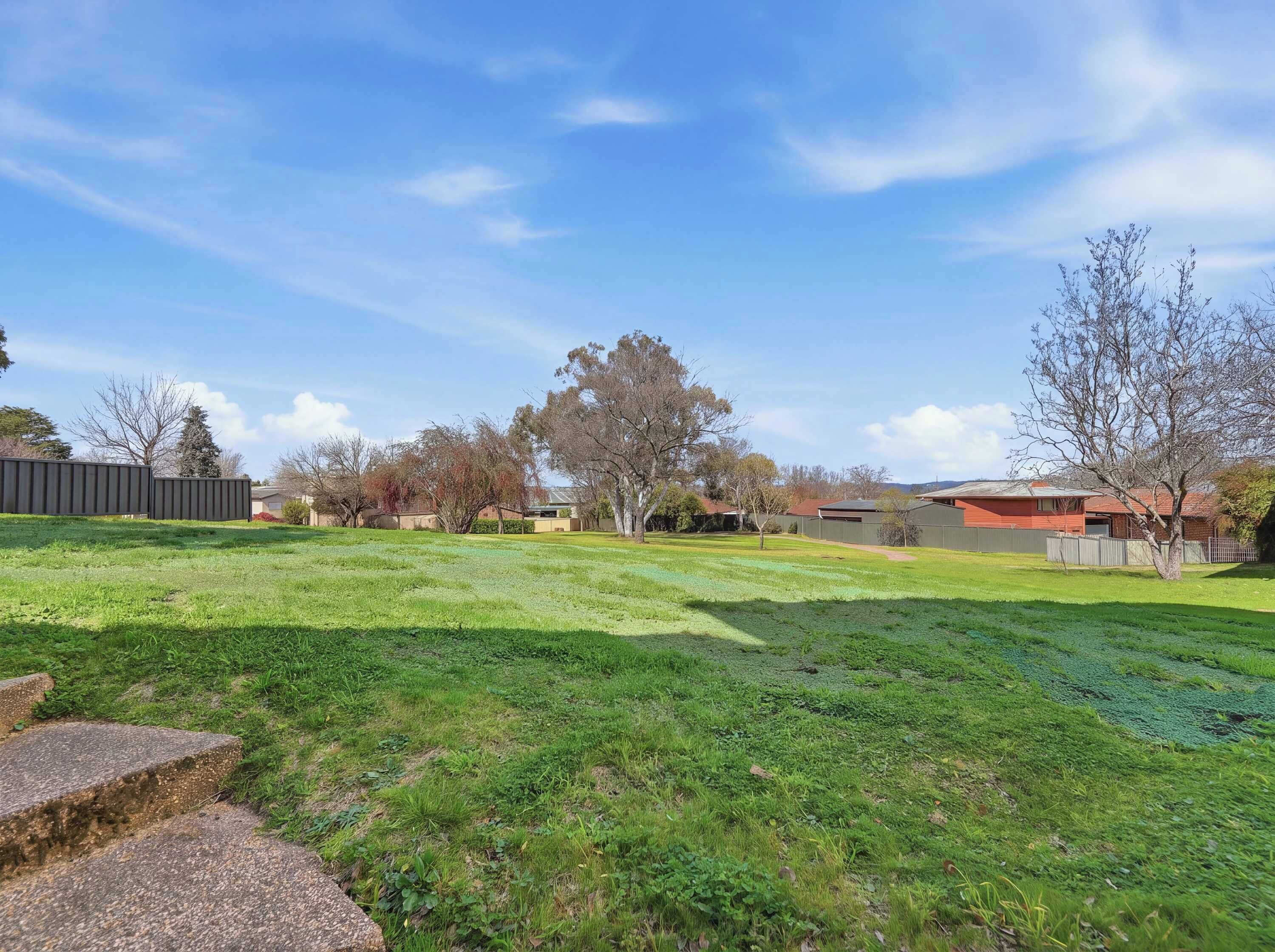 A residential area with a grassy lawn, a paved pathway, and houses in the background.