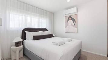 Ein Hotelzimmer mit Bett, Nachttisch, Lampe, einem Gemälde und einer Klimaanlage.