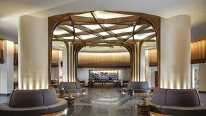 Een moderne lobby met een centraal zitgedeelte, een receptiebalie en een groot kunstwerk aan de muur.