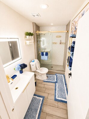 A modern bathroom with a glass shower enclosure, a toilet, and a sink with a mirror. - Ascended Retreat (Dallas)