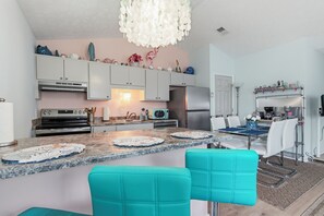 Una cocina moderna con una isla central, armarios blancos, electrodomésticos de acero inoxidable y un comedor con sillas color turquesa.