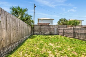 A fenced backyard with grass, a wooden fence, and a house in the background. - So Cute! WALK to Beach Close to Restaurants Marina & State Park Fenced 4 Ur Dog! (Panama City Beach)