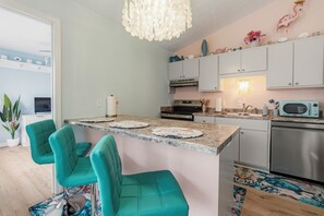 Cozinha com cadeiras verde-água, uma ilha central e um micro-ondas.