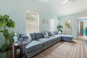 A living room with a sectional sofa, a floor lamp, and a large potted plant. - So Cute! WALK to Beach Close to Restaurants Marina & State Park Fenced 4 Ur Dog! (Panama City Beach)