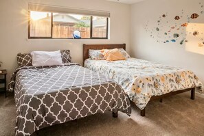 A bedroom with two beds, a window, and a wall with fish decals.