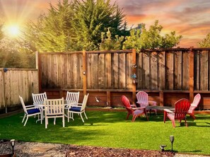 Een achtertuin met een houten schutting, een gazon en tuinmeubilair, waaronder stoelen en een tafel.