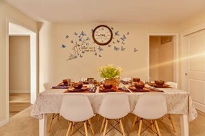 A dining room with a table set for four, a clock on the wall, and butterfly decals.