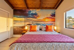 Een slaapkamer met een groot bed, een muurschildering van een zonsondergang en een raam met uitzicht.