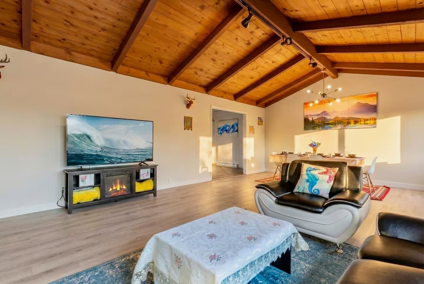 Een ruime woonkamer met houten balkenplafond, een open haard, een televisie en een eethoek.