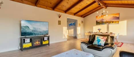 Un salon spacieux avec un plafond en bois, une cheminée, un téléviseur et un coin repas.