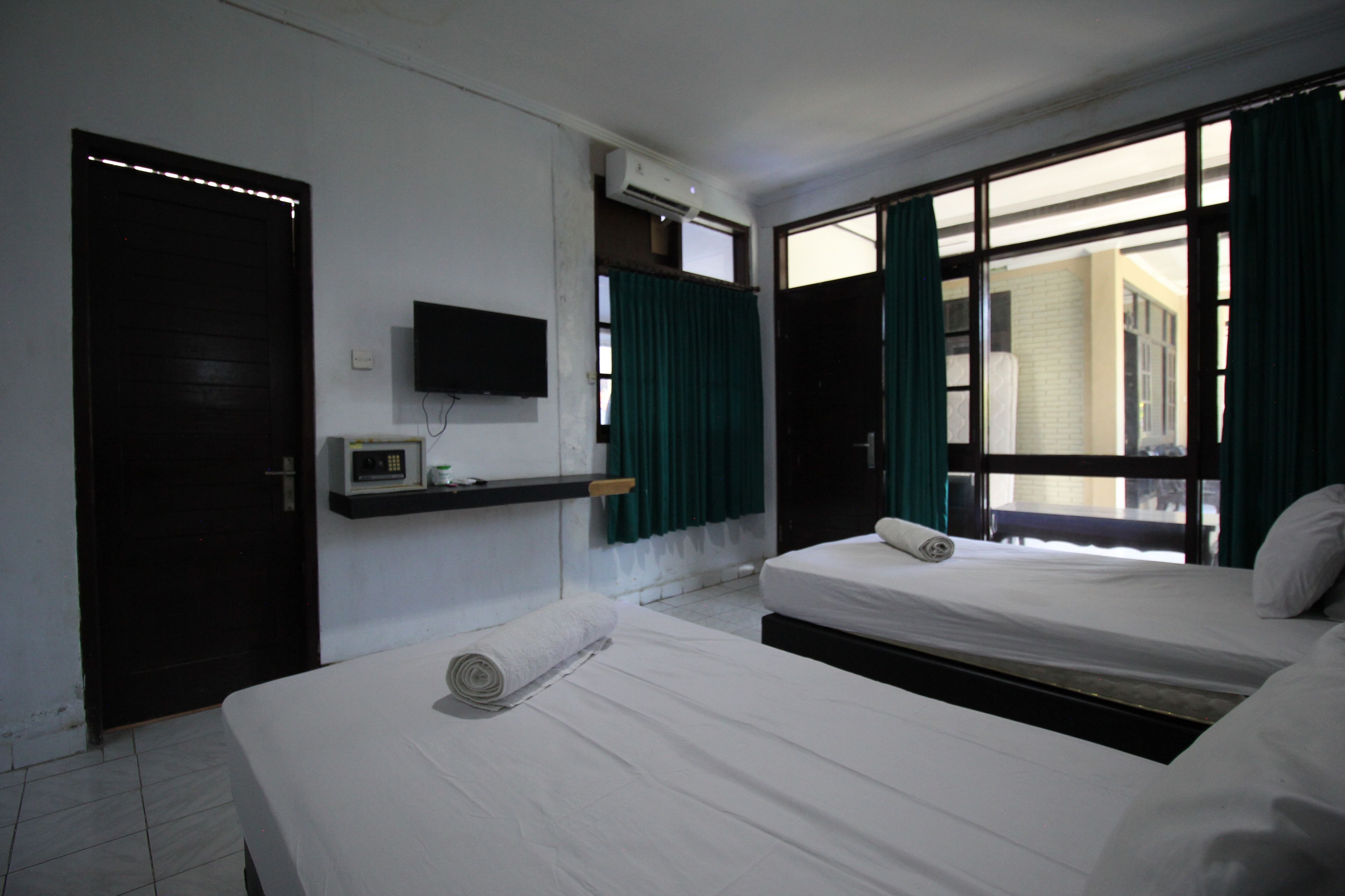 A hotel room with two beds, a TV, an air conditioning unit, and a window with curtains.