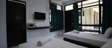 A hotel room with two beds, a TV, an air conditioning unit, and a window with curtains.