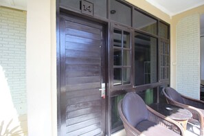 A dark wooden door with a number plate, a glass window, and two wicker chairs with cushions outside a building. - Moanna Stay Kuta Beach (Kuta)