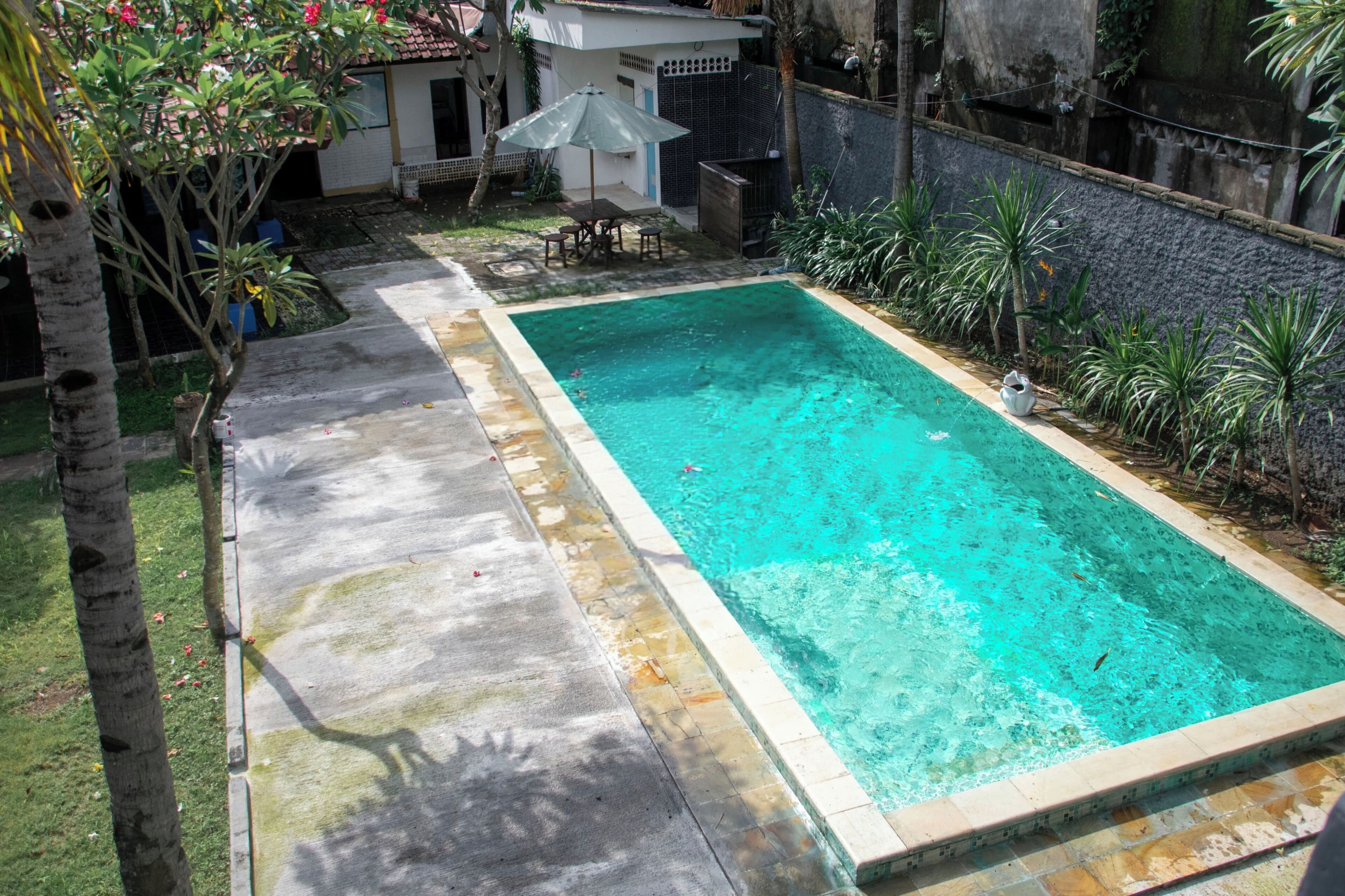 Ein rechteckiger Pool mit einer gefliesten Kante, umgeben von einer Betonplattform und einer niedrigen Steinmauer.