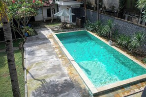 A rectangular swimming pool with a tiled edge, surrounded by a concrete deck and a low stone wall. - Moanna Stay Kuta Beach (Kuta)