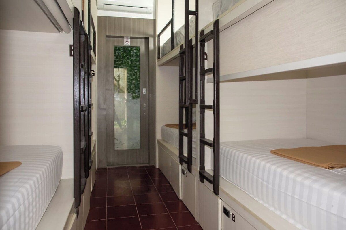A narrow corridor with bunk beds on either side, a door at the end, and a tiled floor.