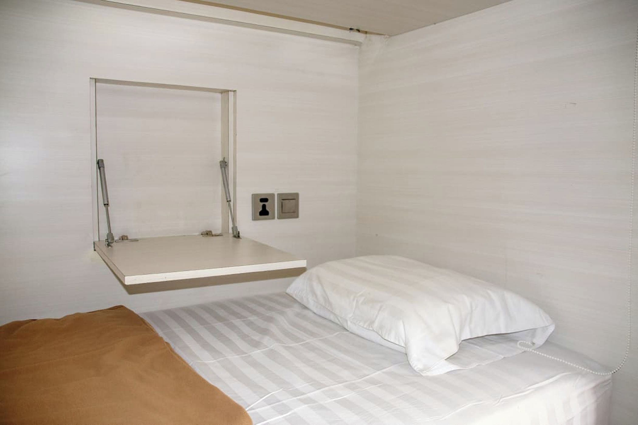 Ein kleines Zimmer mit einem Einzelbett, einer Hantelstange und einem Nachttisch.