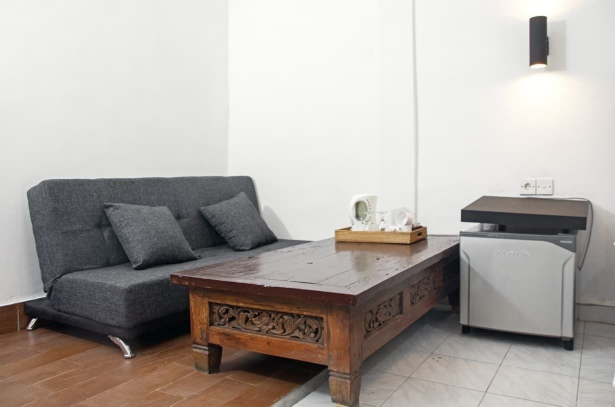 A room with a grey sofa, a wooden coffee table, a white refrigerator, and a wall-mounted light fixture.
