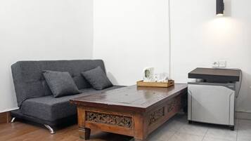 A room with a grey sofa, a wooden coffee table, a white refrigerator, and a wall-mounted light fixture.