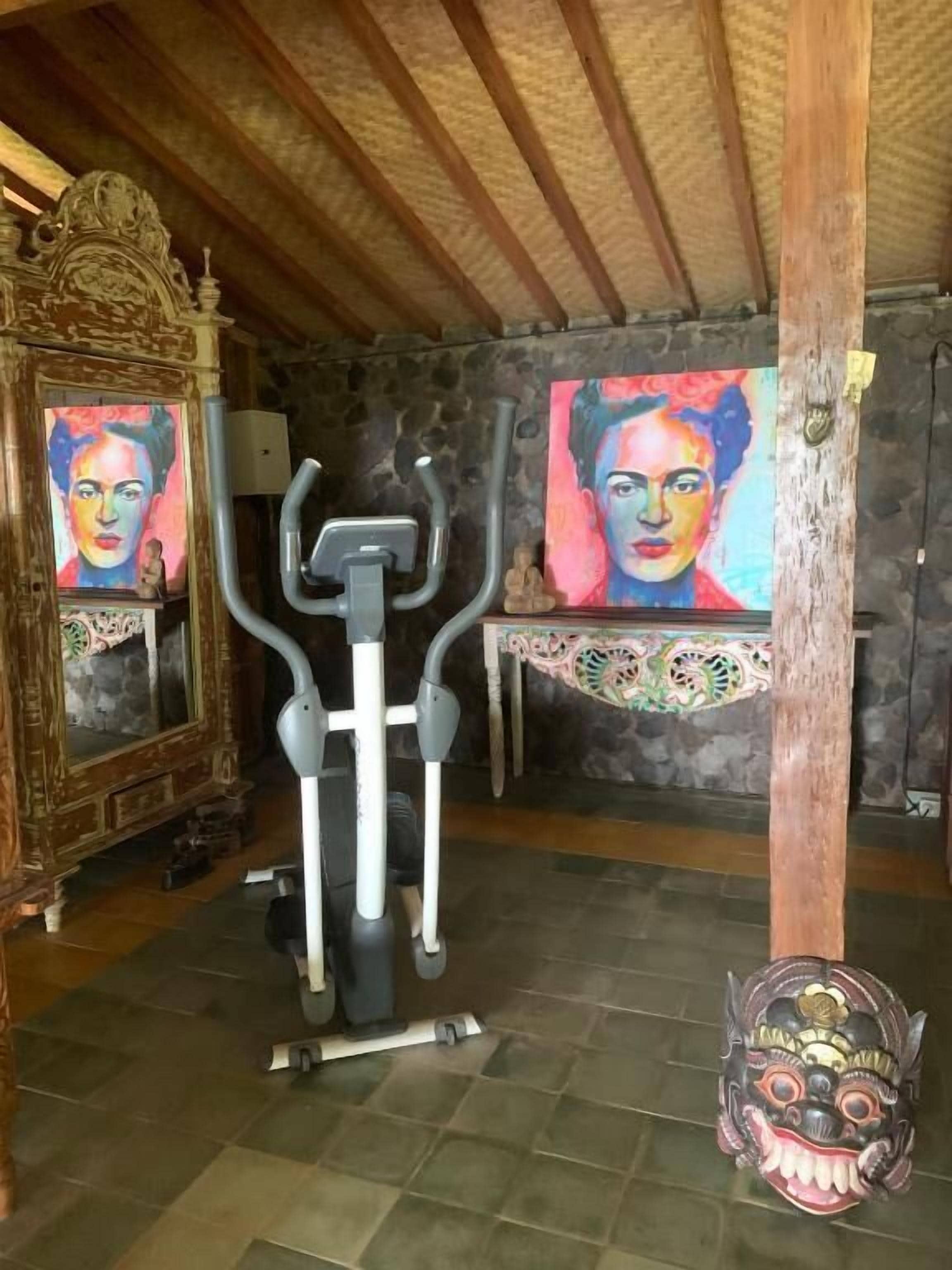 A room with a treadmill, a wooden ceiling, a stone wall, and a decorative mask.