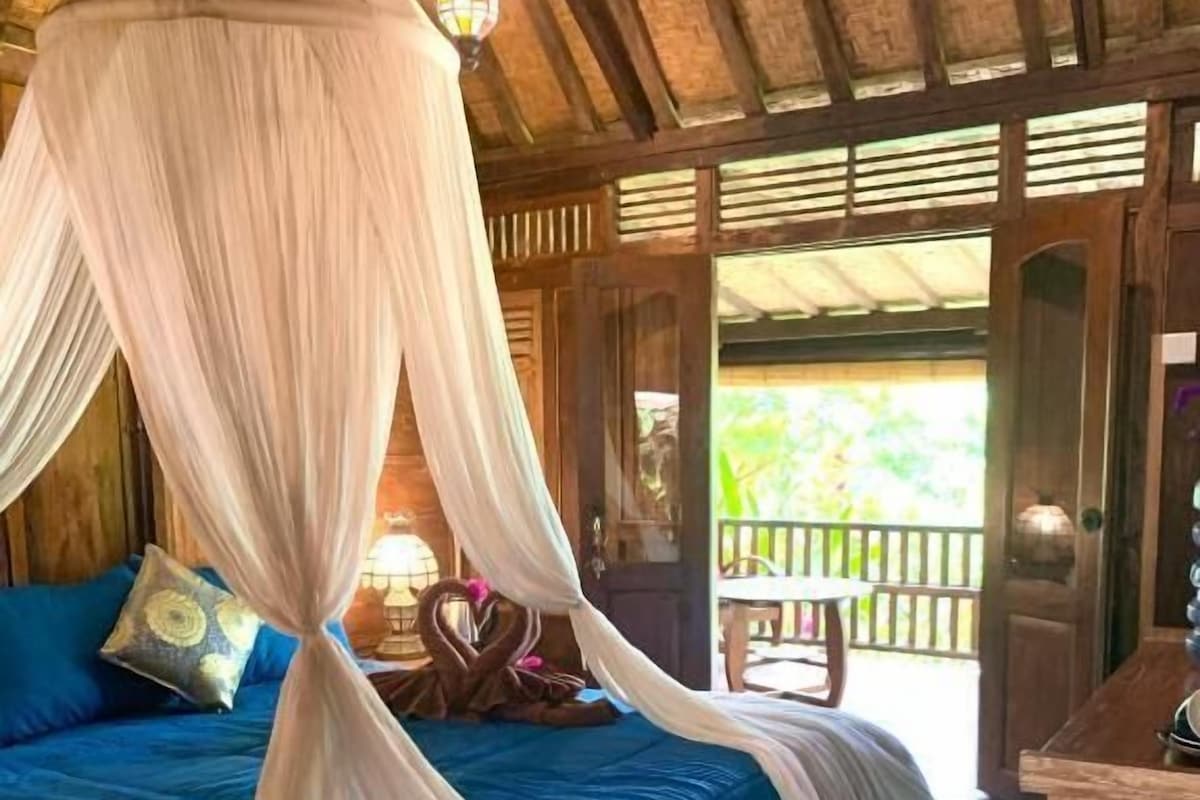 A room with a bed, a wooden table, and a balcony with a railing.
