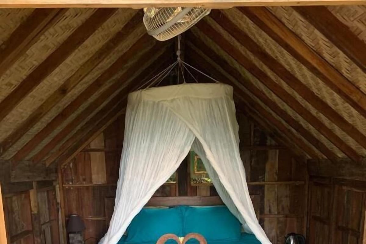 A single bed with a canopy, a heart-shaped decoration on the bedspread, and a wooden floor.