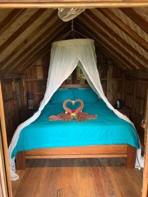 Una cama individual con dosel, un adorno con forma de corazón en la colcha y suelo de madera.