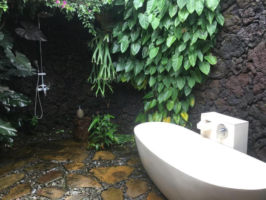 Un baño con piso de piedra, una bañera blanca y una pared cubierta de follaje verde.