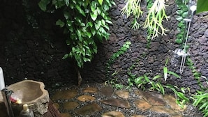 Piso de baldosas de piedra, pared de piedra rústica y follaje verde.