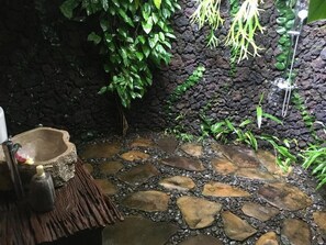 A stone-tiled floor with a rustic stone wall and green foliage. - villa kepuh (buleleng)