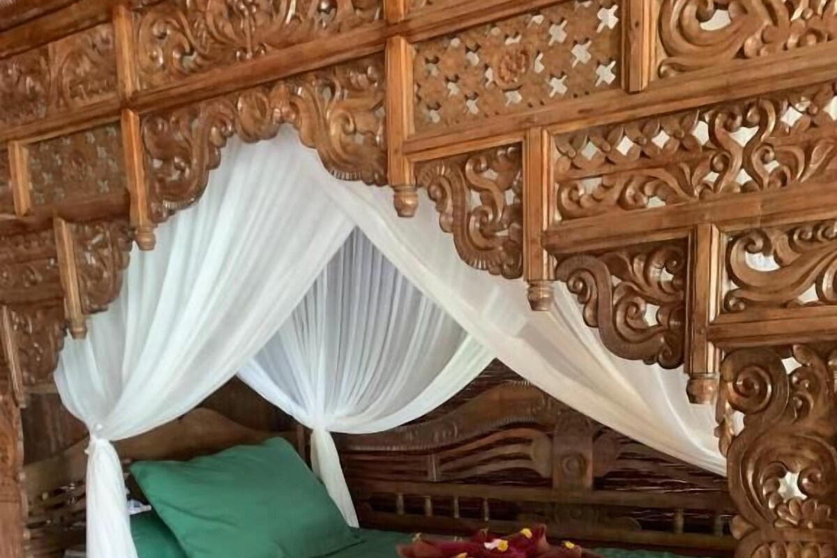 A wooden bed with a canopy, green bedding, and a decorative headboard.
