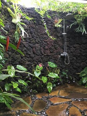 A stone wall with a showerhead, surrounded by lush green plants. - villa kepuh (buleleng)