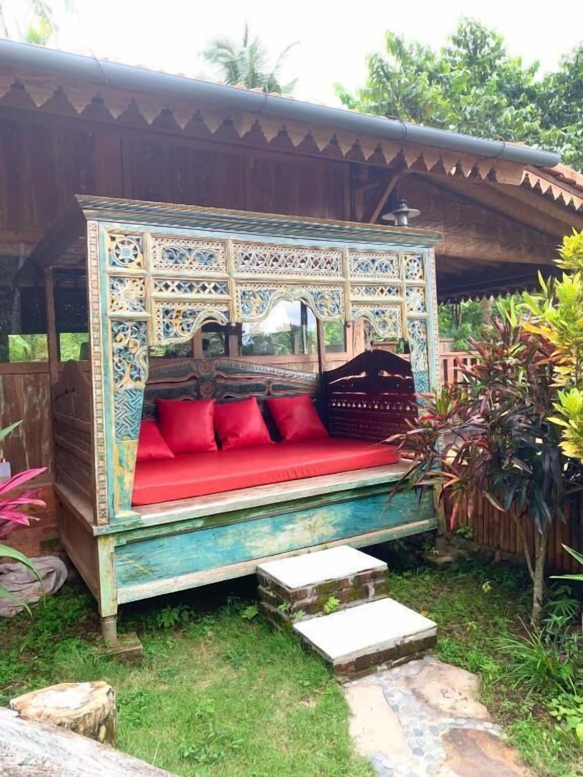 Un banco de madera con diseños intrincados, cojines rojos y una pequeña mesa con una lámpara.