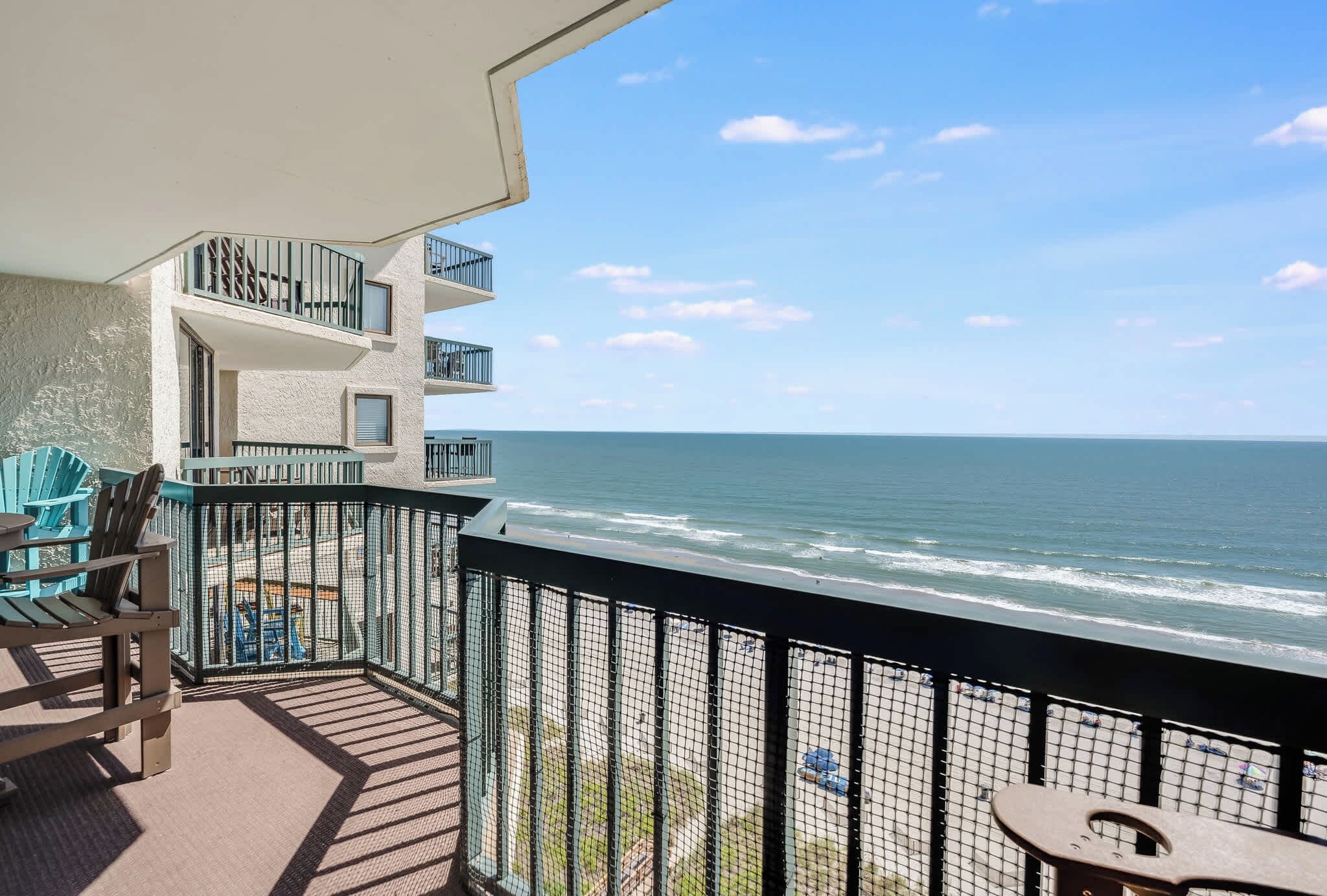 Een balkon met uitzicht op de oceaan, een zithoek met stoelen, en een gebouw met meerdere balkons.